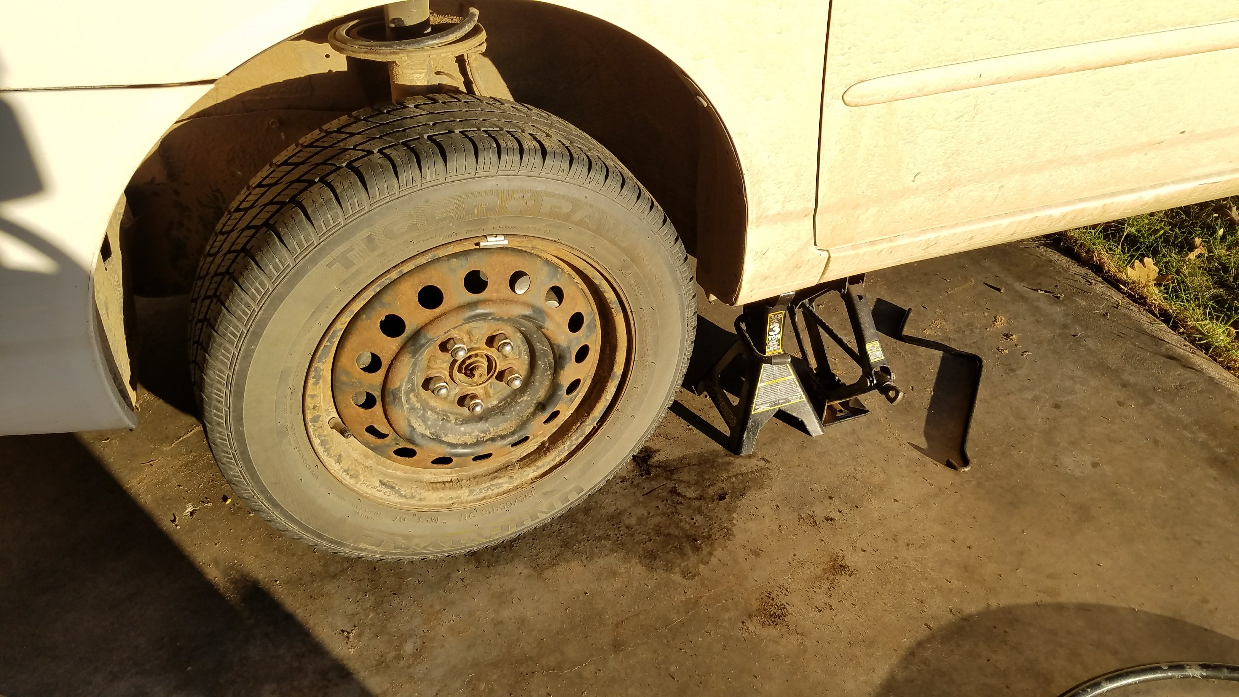 A toyota corolla jacked up using the stock jack and with a jackstand for safety.